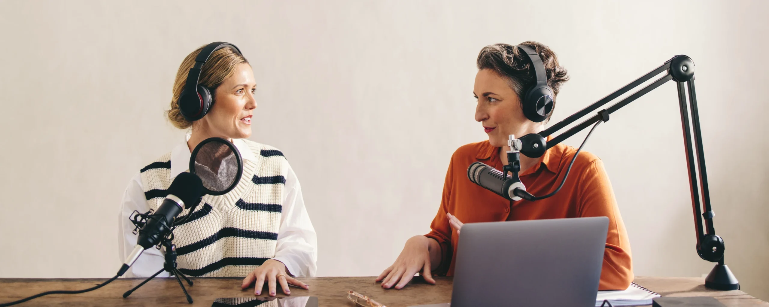 Two women are sitting at a table with headphones on.